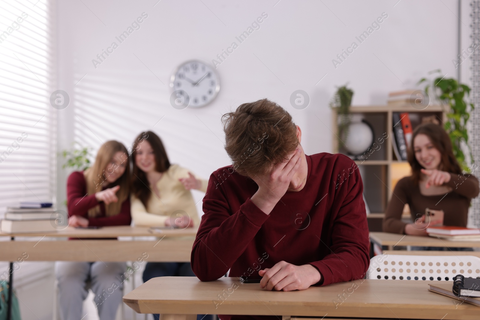 Cyber bullying. Upset teenage boy with smartphone and schoolmates pointing at him in classroom, selective focus Photo of Cyber bullying. Upset teenage boy with smartphone and schoolmates pointing at him in classroom, selective focus