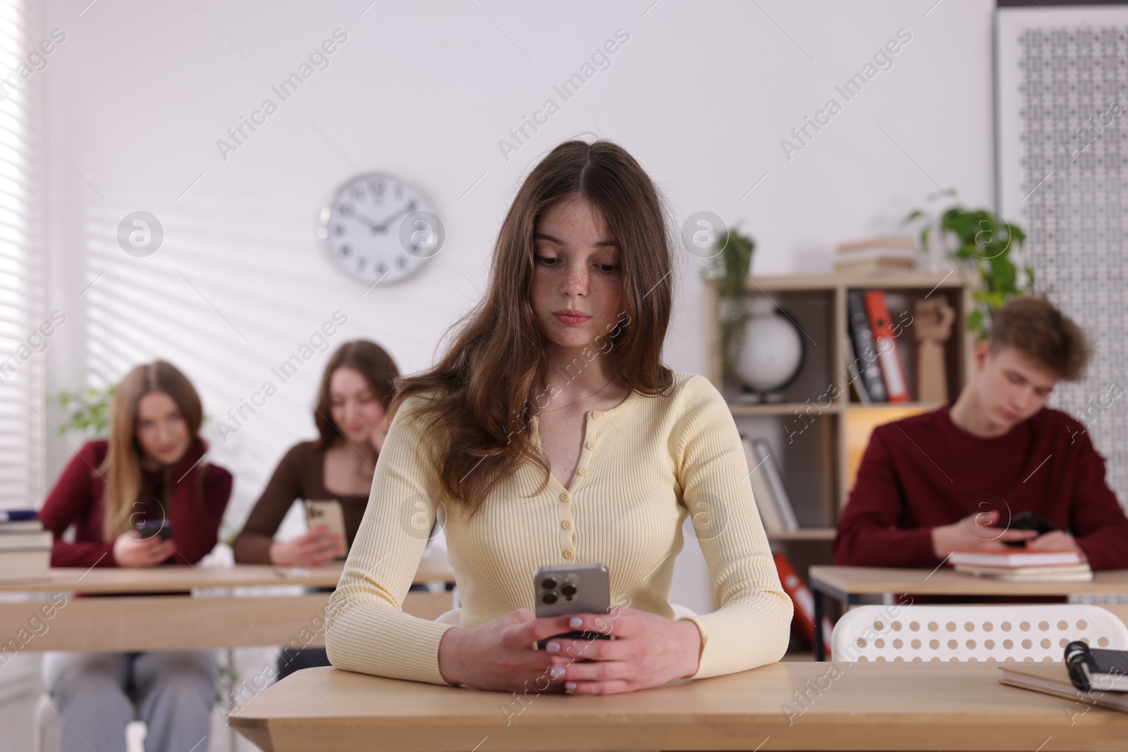 Cyber bullying. Upset teenage girl with smartphone at desk in classroom Photo of Cyber bullying. Upset teenage girl with smartphone at desk in classroom