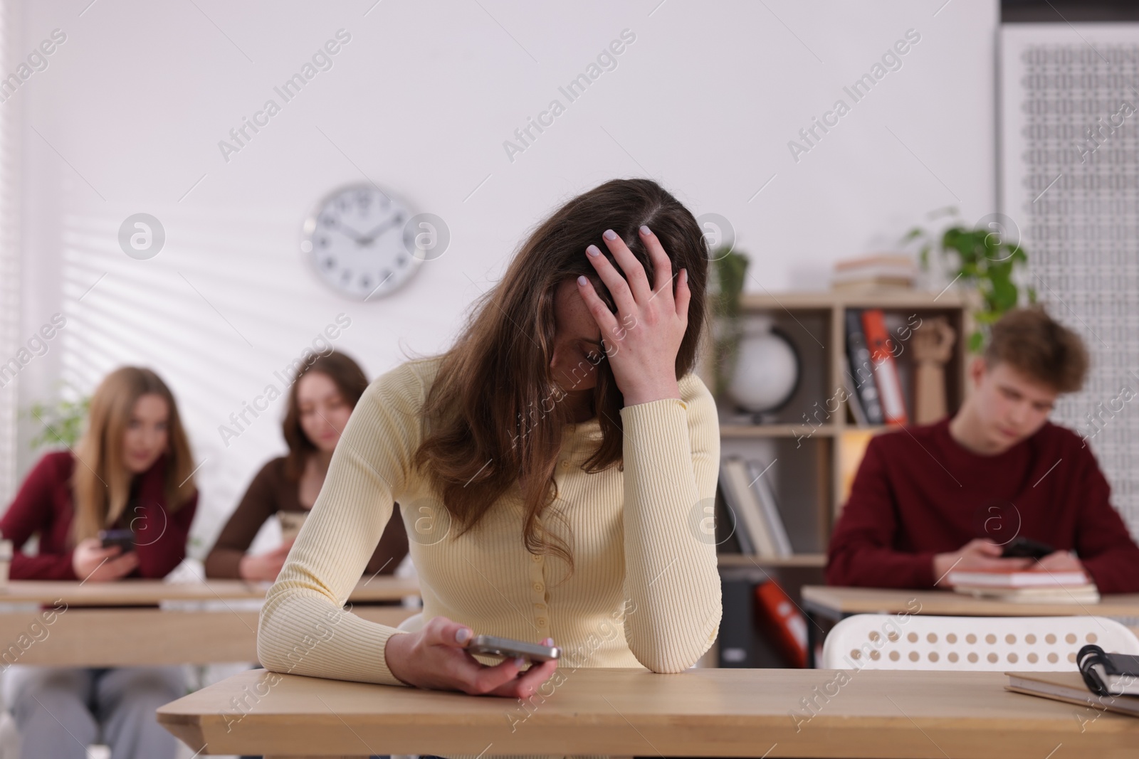 Cyber bullying. Upset teenage girl with smartphone at desk in classroom Photo of Cyber bullying. Upset teenage girl with smartphone at desk in classroom