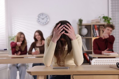 Photo of Cyber bullying. Upset teenage girl with smartphone and schoolmates pointing at her in classroom, selective focus