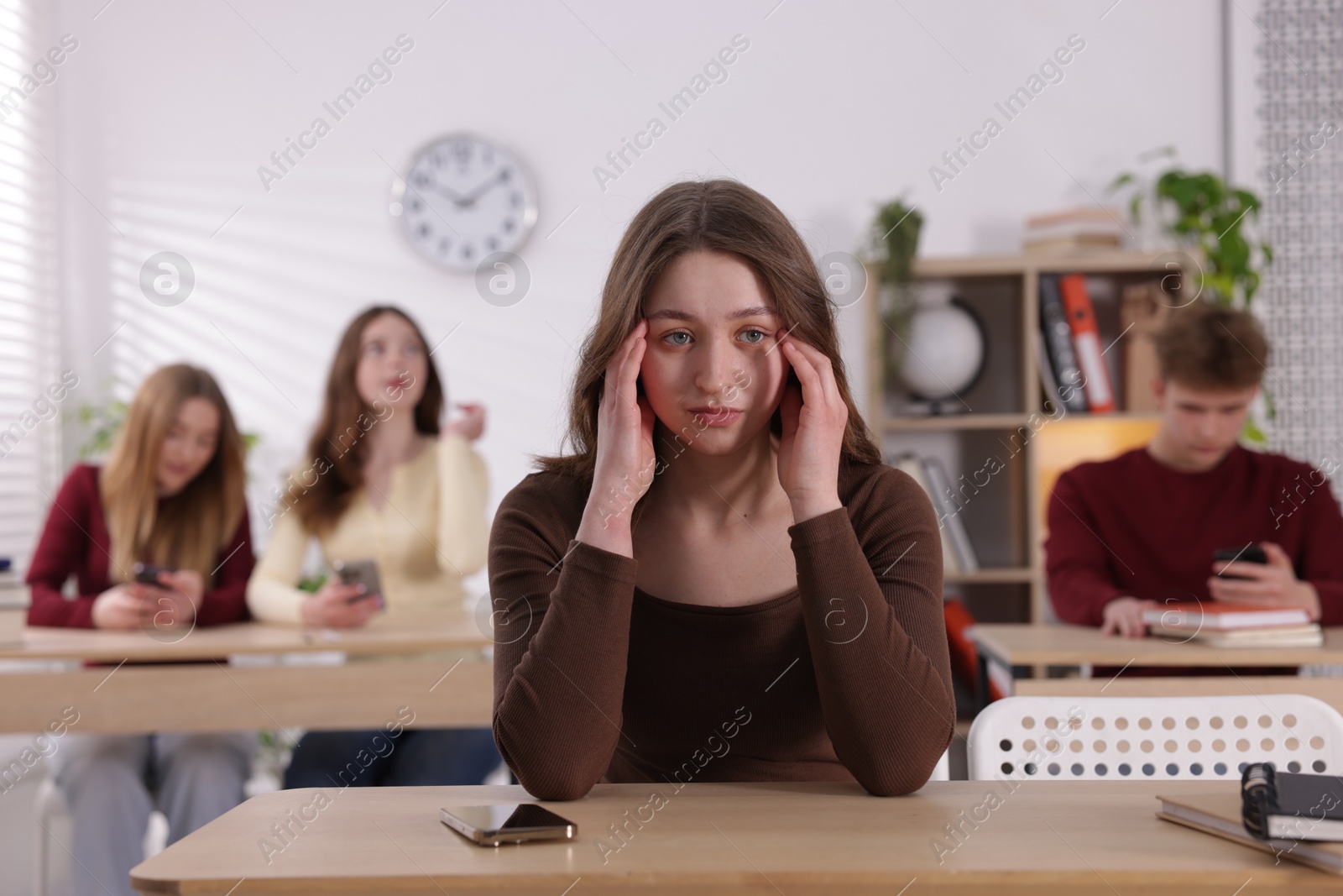Cyber bullying. Upset teenage girl with smartphone at desk in classroom Photo of Cyber bullying. Upset teenage girl with smartphone at desk in classroom