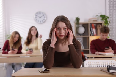 Photo of Cyber bullying. Upset teenage girl with smartphone at desk in classroom