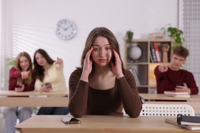 Photo of Cyber bullying. Upset teenage girl with smartphone and schoolmates pointing at her in classroom, selective focus