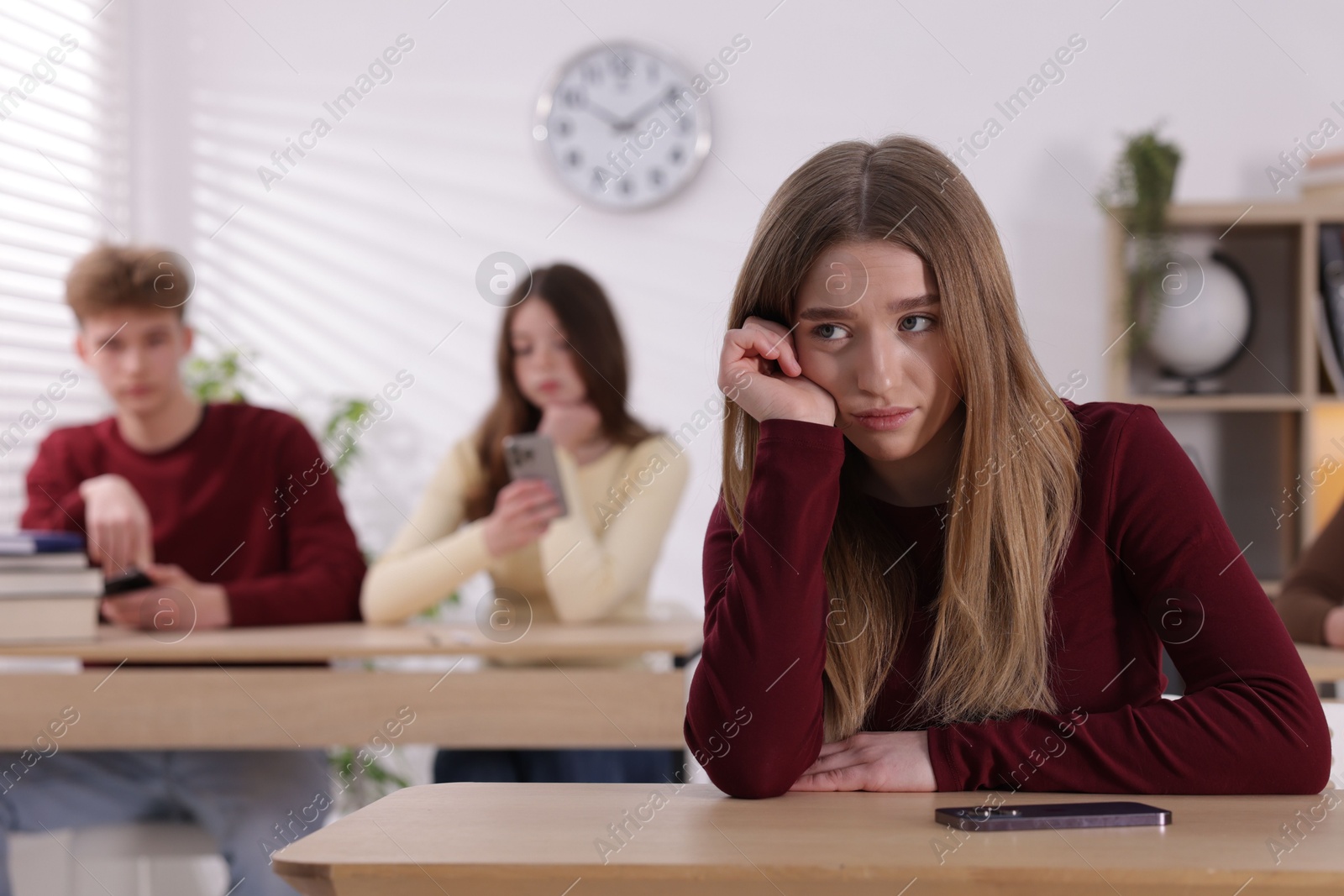 Cyber bullying. Upset teenage girl with smartphone at desk in classroom Photo of Cyber bullying. Upset teenage girl with smartphone at desk in classroom
