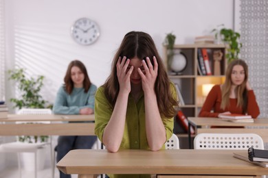 Photo of Bullying. Upset teenage girl at desk in school