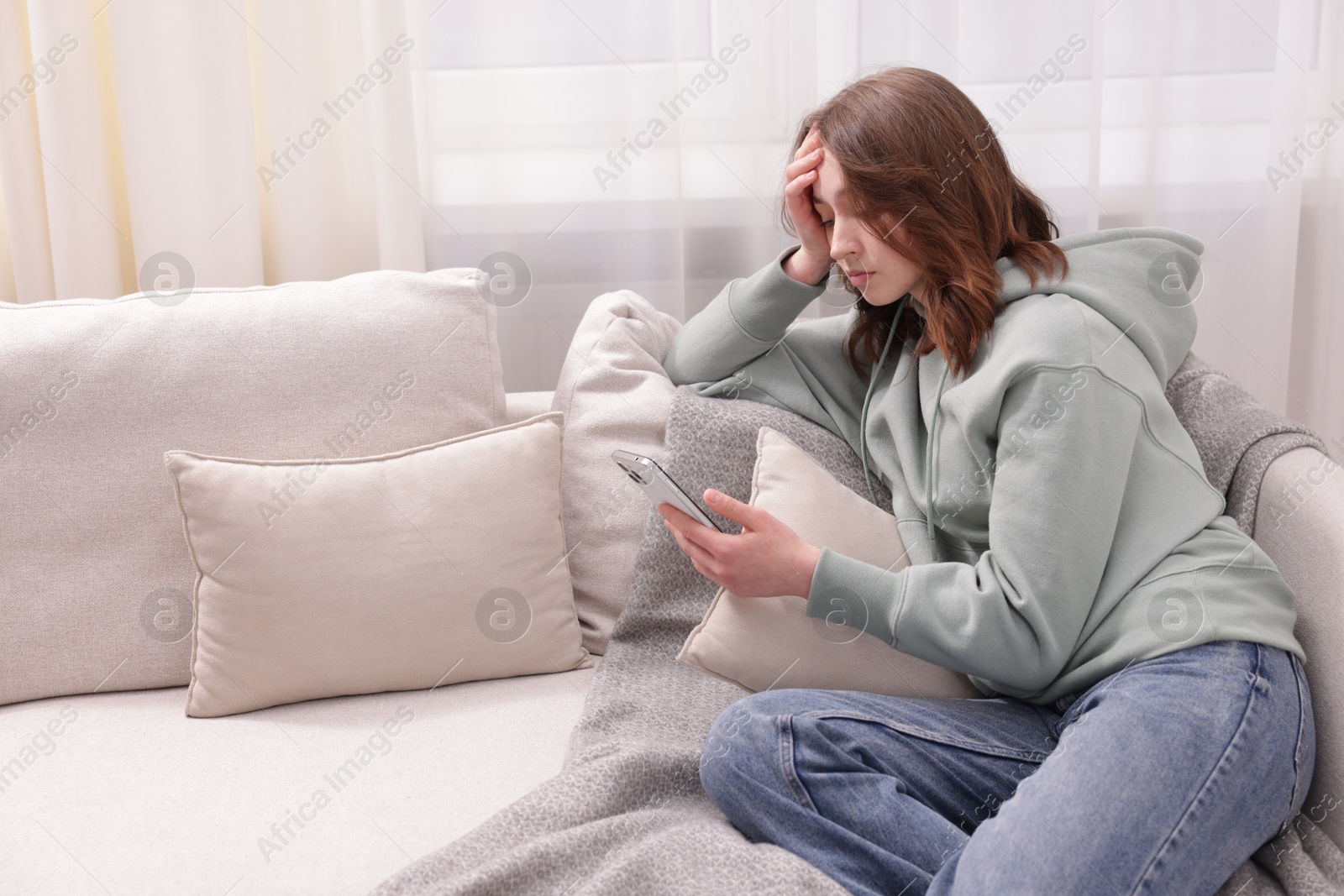 Cyber bullying. Upset teenage girl with smartphone on sofa at home. Space for text Photo of Cyber bullying. Upset teenage girl with smartphone on sofa at home. Space for text