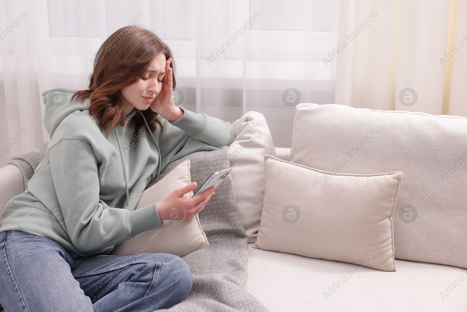 Cyber bullying. Upset teenage girl with smartphone on sofa at home. Space for text Photo of Cyber bullying. Upset teenage girl with smartphone on sofa at home. Space for text