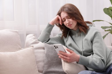 Photo of Cyber bullying. Upset teenage girl with smartphone on sofa at home