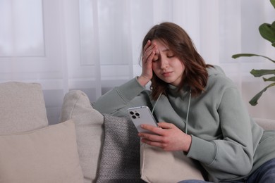 Photo of Cyber bullying. Upset teenage girl with smartphone on sofa at home. Space for text