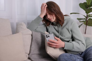 Photo of Cyber bullying. Upset teenage girl with smartphone on sofa at home. Space for text