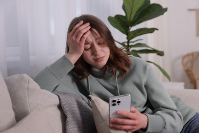 Photo of Cyber bullying. Upset teenage girl with smartphone on sofa at home