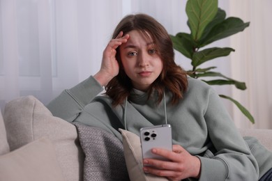 Photo of Cyber bullying. Upset teenage girl with smartphone on sofa at home
