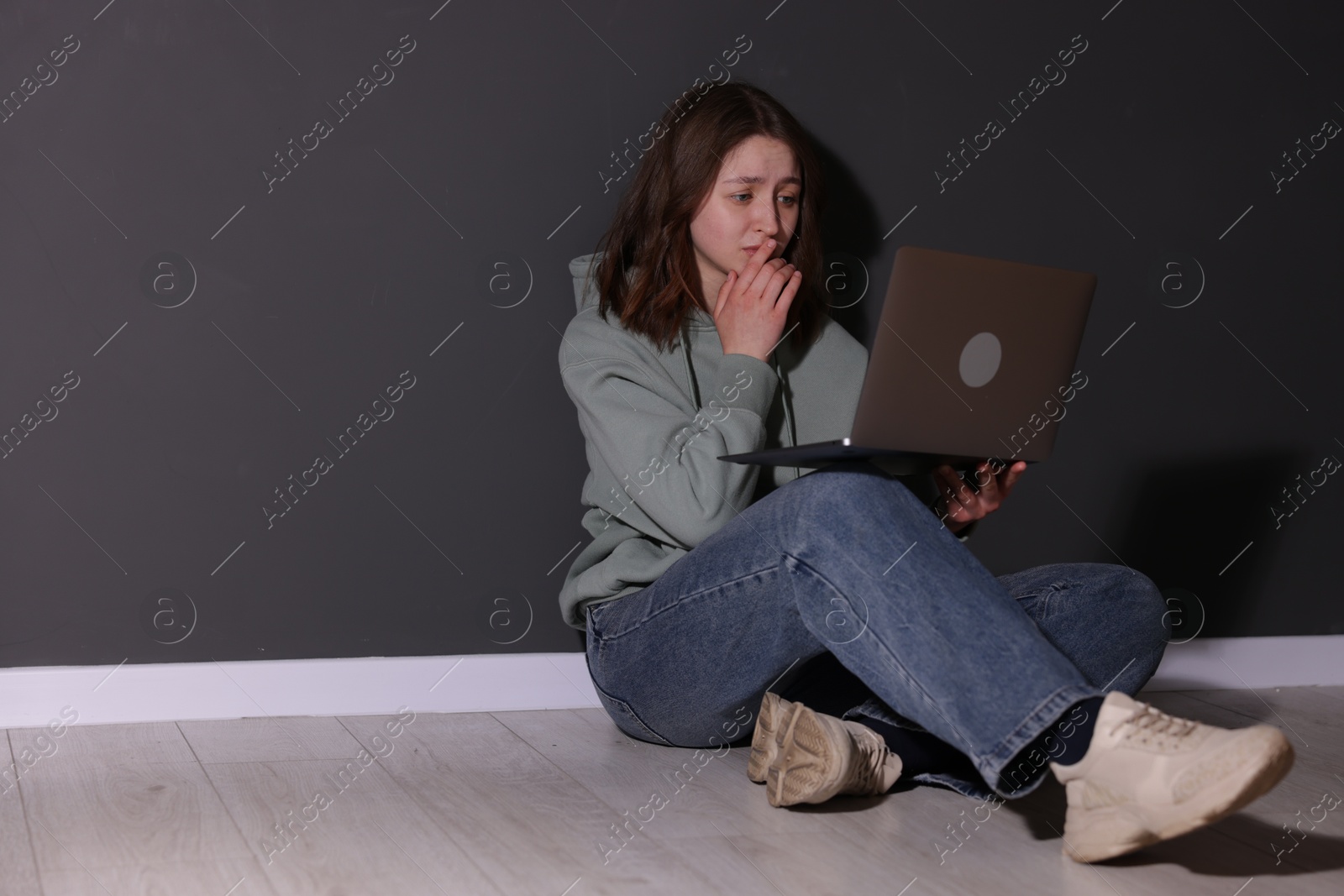 Cyber bullying. Upset teenage girl with laptop on floor indoors. Space for text Photo of Cyber bullying. Upset teenage girl with laptop on floor indoors. Space for text