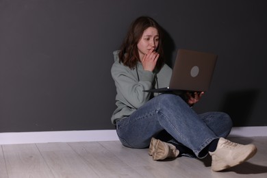 Photo of Cyber bullying. Upset teenage girl with laptop on floor indoors. Space for text