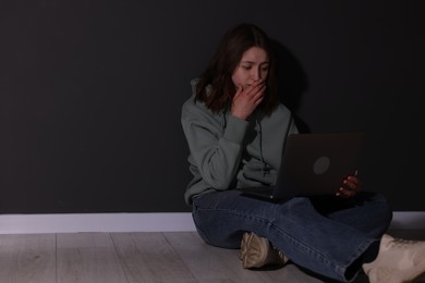 Photo of Cyber bullying. Upset teenage girl with laptop on floor indoors. Space for text