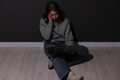 Photo of Cyber bullying. Upset teenage girl with laptop on floor indoors
