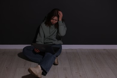 Photo of Cyber bullying. Upset teenage girl with laptop on floor indoors. Space for text
