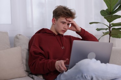 Photo of Cyber bullying. Upset teenage boy with laptop on sofa indoors