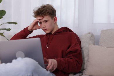 Photo of Cyber bullying. Upset teenage boy with laptop on sofa indoors