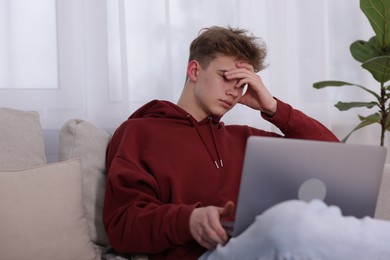 Photo of Cyber bullying. Upset teenage boy with laptop on sofa indoors