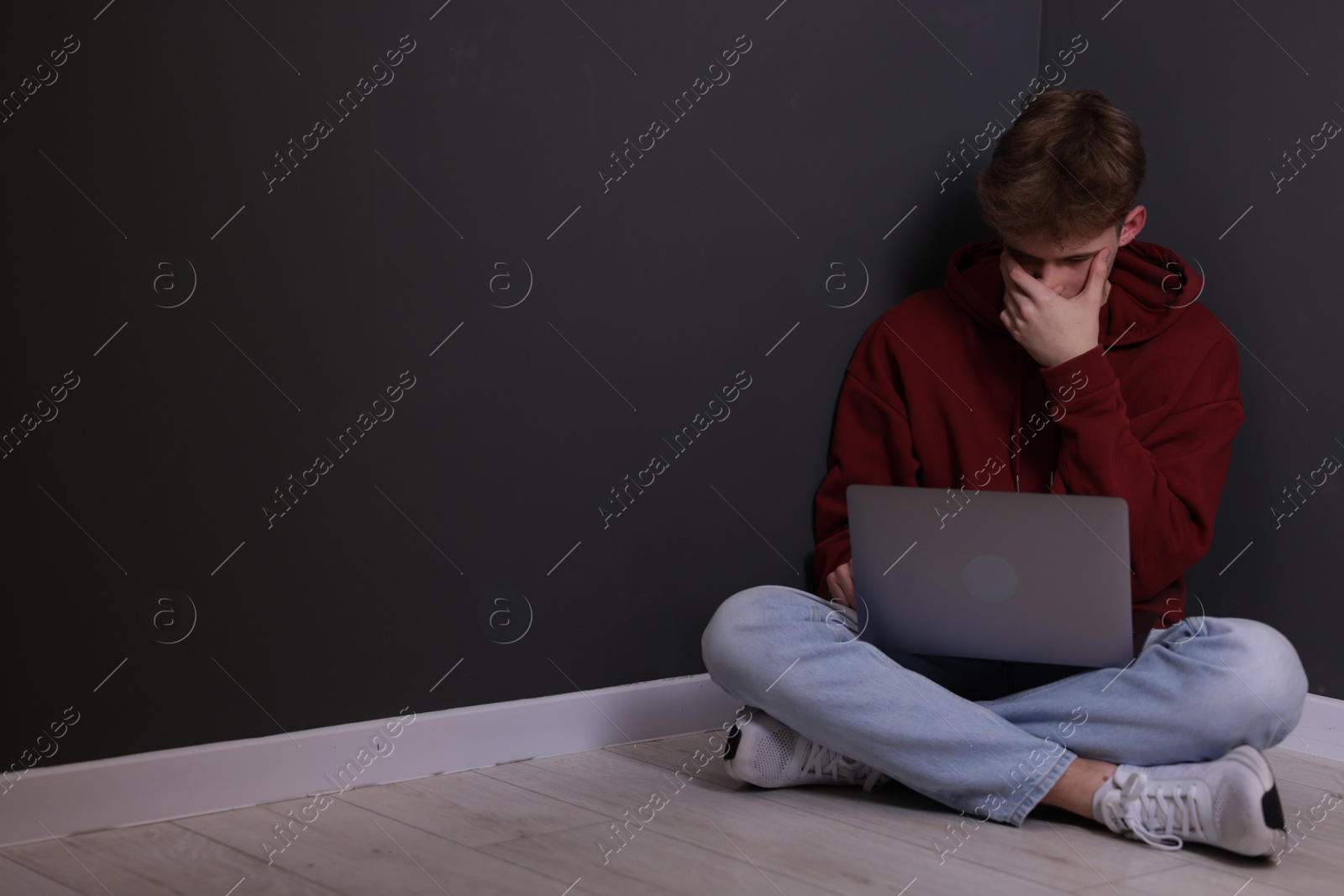 Cyber bullying. Upset teenage boy with laptop on floor indoors. Space for text Photo of Cyber bullying. Upset teenage boy with laptop on floor indoors. Space for text