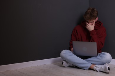 Photo of Cyber bullying. Upset teenage boy with laptop on floor indoors. Space for text