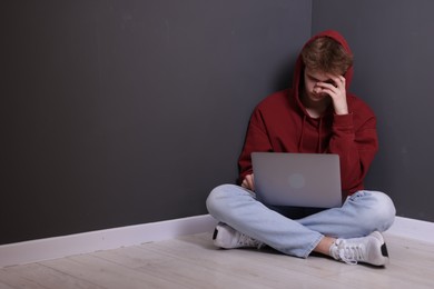Photo of Cyber bullying. Upset teenage boy with laptop on floor indoors. Space for text