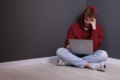Photo of Cyber bullying. Upset teenage boy with laptop on floor indoors. Space for text