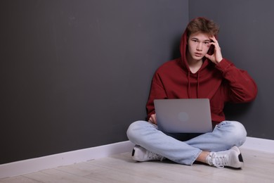 Photo of Cyber bullying. Upset teenage boy with laptop on floor indoors. Space for text