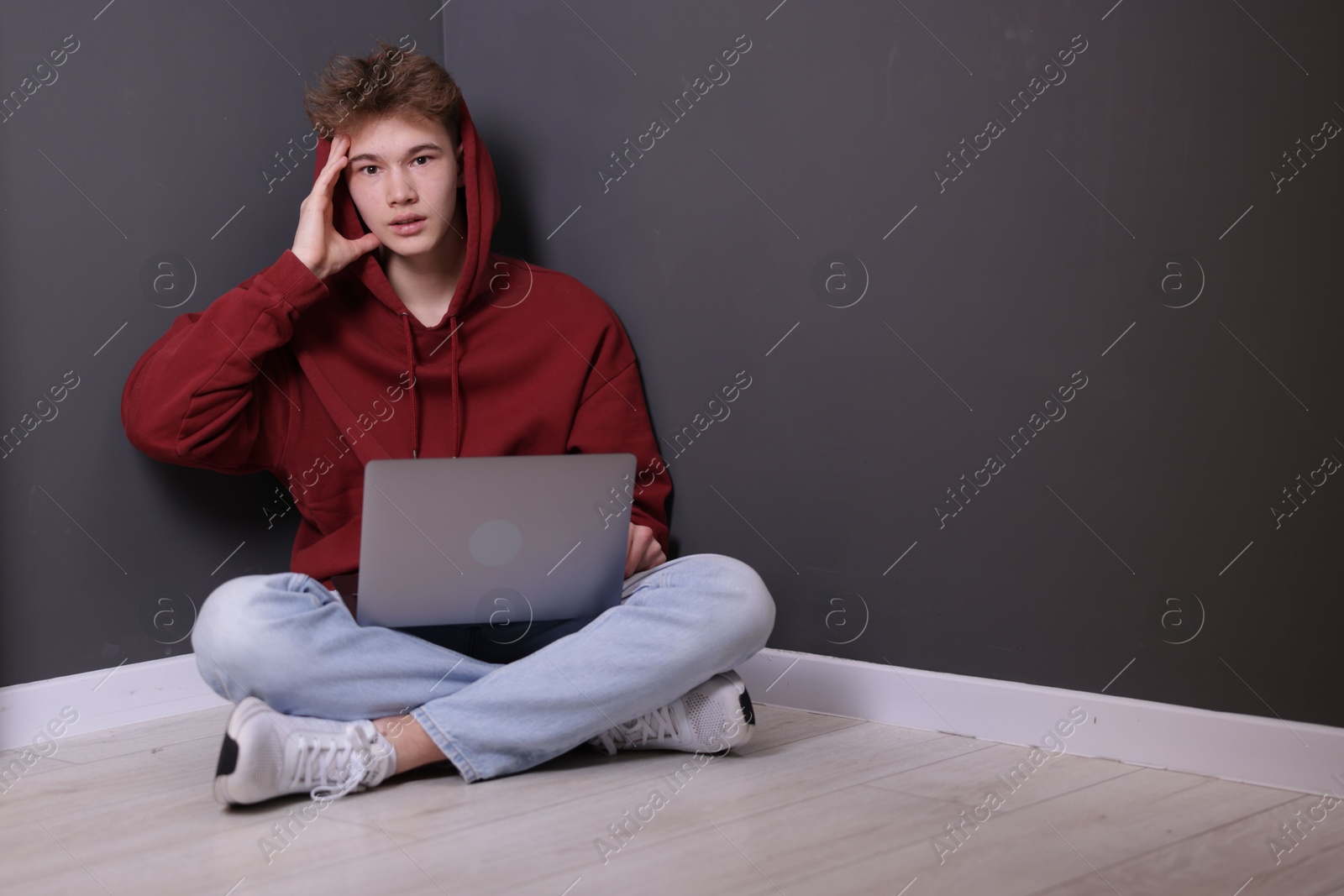 Cyber bullying. Upset teenage boy with laptop on floor indoors. Space for text Photo of Cyber bullying. Upset teenage boy with laptop on floor indoors. Space for text