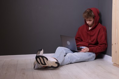 Photo of Cyber bullying. Upset teenage boy with laptop on floor indoors. Space for text