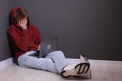 Photo of Cyber bullying. Upset teenage boy with laptop on floor indoors. Space for text