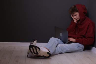 Photo of Cyber bullying. Upset teenage boy with laptop on floor indoors. Space for text
