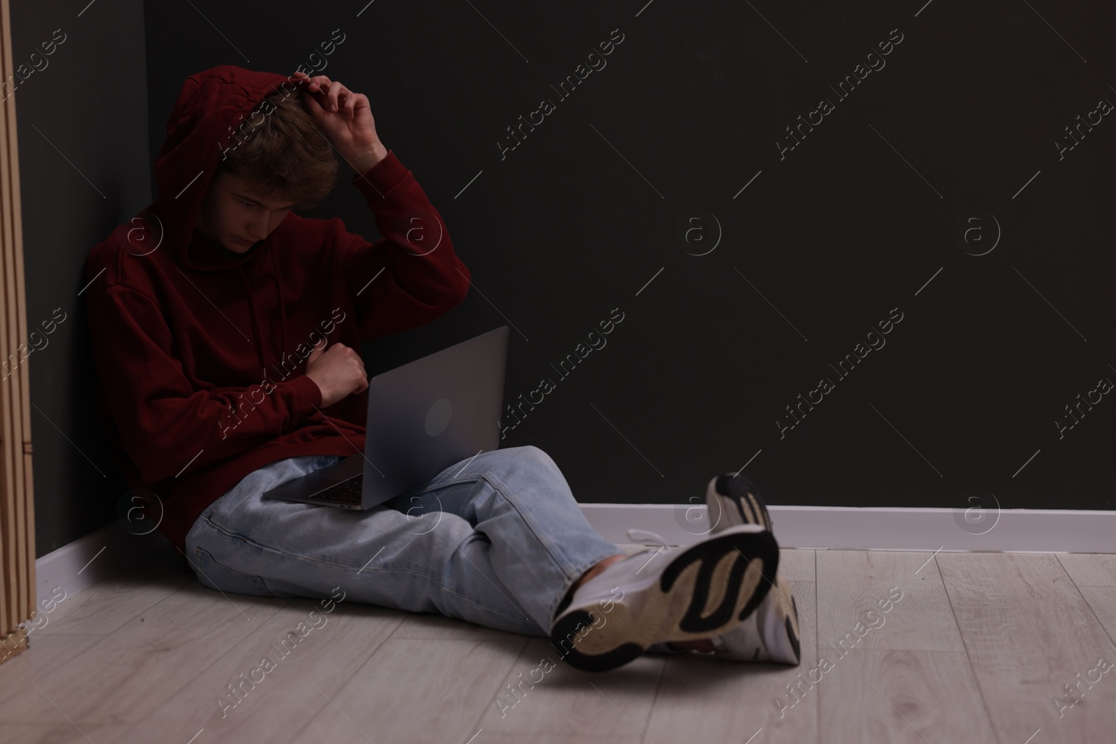 Cyber bullying. Upset teenage boy with laptop on floor indoors. Space for text Photo of Cyber bullying. Upset teenage boy with laptop on floor indoors. Space for text