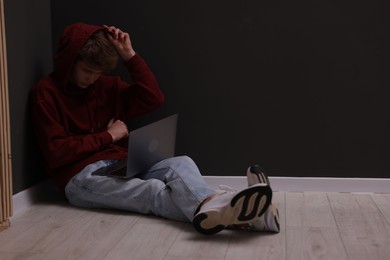 Photo of Cyber bullying. Upset teenage boy with laptop on floor indoors. Space for text