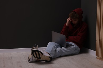 Photo of Cyber bullying. Upset teenage boy with laptop on floor indoors. Space for text