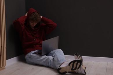 Photo of Cyber bullying. Upset teenage boy with laptop on floor indoors. Space for text