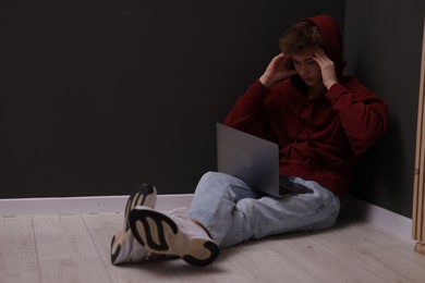 Photo of Cyber bullying. Upset teenage boy with laptop on floor indoors. Space for text