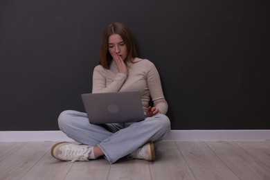 Photo of Cyber bullying. Upset teenage girl with laptop on floor indoors