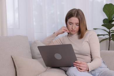 Photo of Cyber bullying. Upset teenage girl with laptop on sofa at home. Space for text