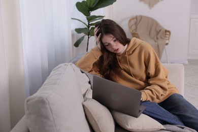 Photo of Cyber bullying. Upset teenage girl with laptop on sofa at home