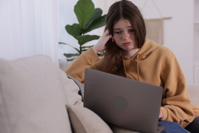 Photo of Cyber bullying. Upset teenage girl with laptop on sofa at home