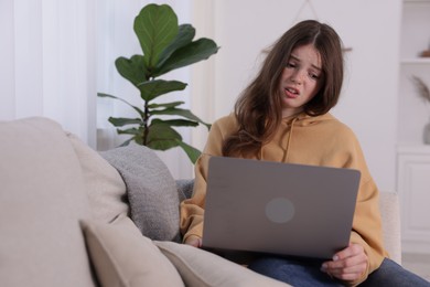 Photo of Cyber bullying. Upset teenage girl with laptop on sofa at home