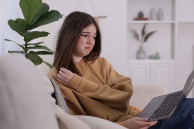 Photo of Cyber bullying. Upset teenage girl with laptop on sofa at home