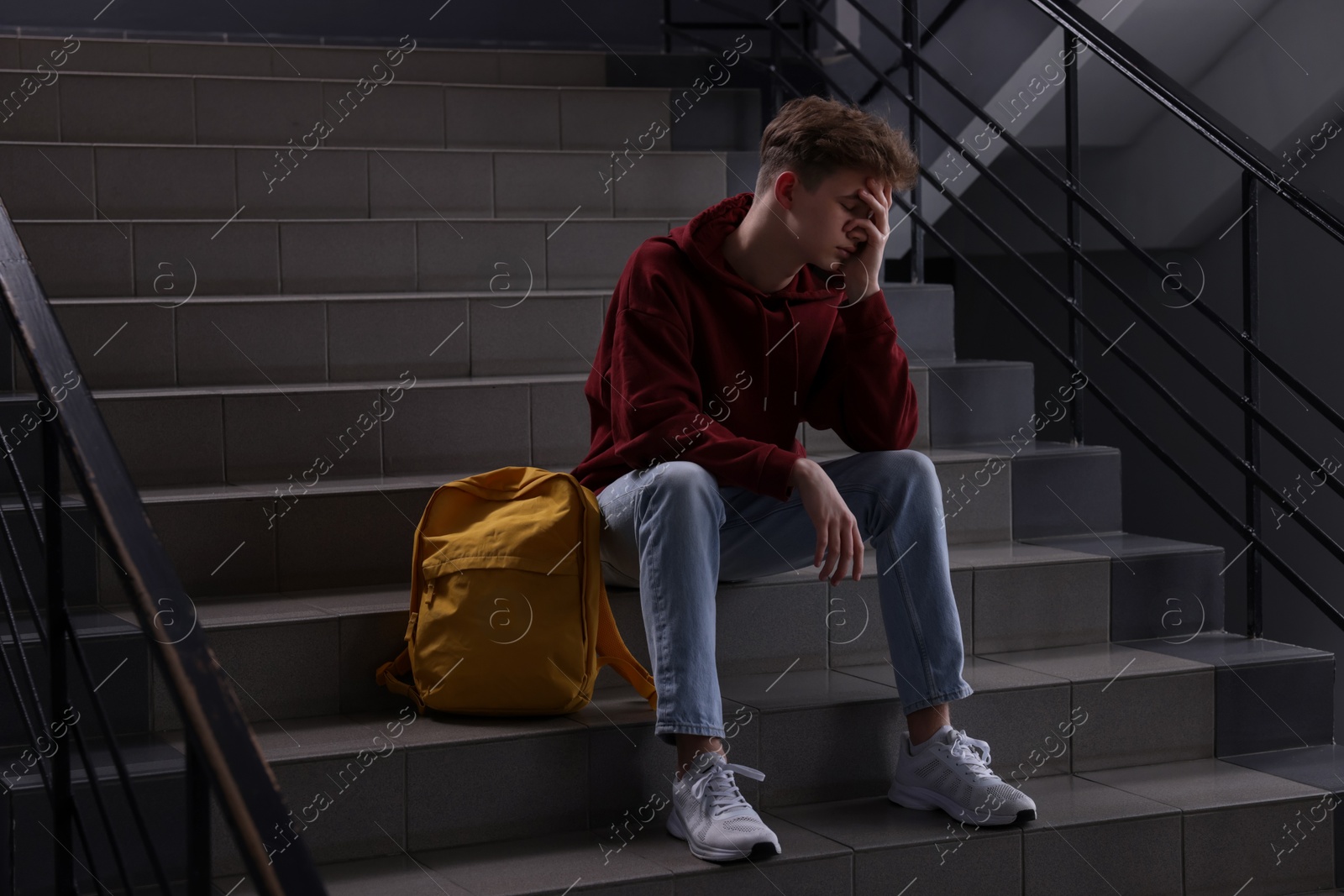 Photo of Bullying. Upset teenage boy on stairs indoors