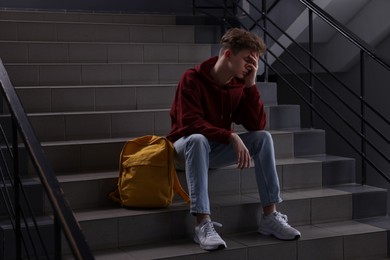 Photo of Bullying. Upset teenage boy on stairs indoors