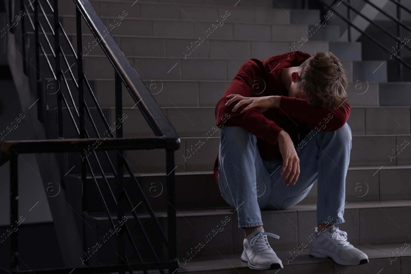 Bullying. Upset teenage boy on stairs indoors. Space for text Photo of Bullying. Upset teenage boy on stairs indoors. Space for text