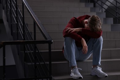 Photo of Bullying. Upset teenage boy on stairs indoors. Space for text