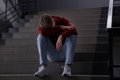 Photo of Bullying. Upset teenage boy on stairs indoors