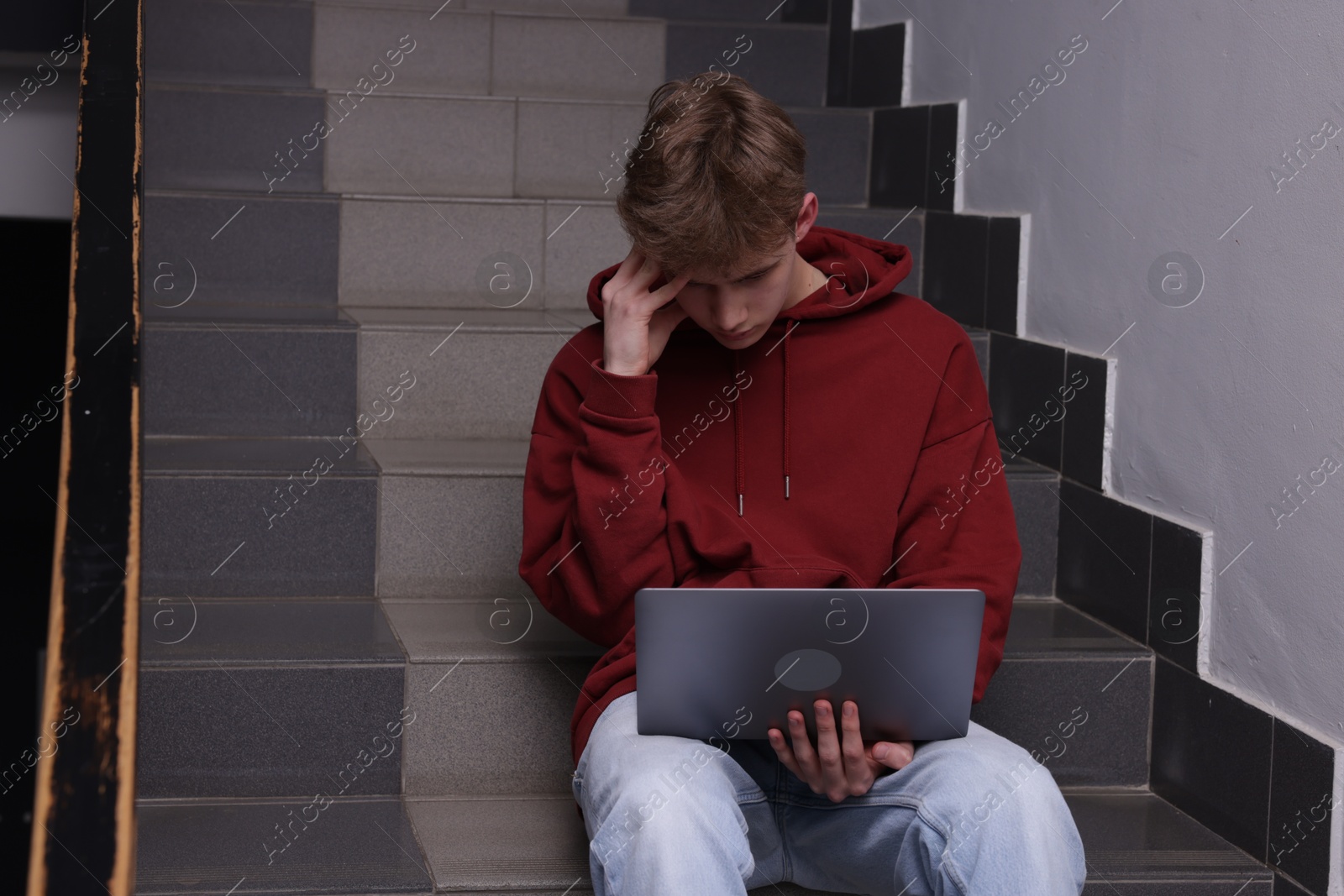 Cyber bullying. Upset teenage boy with laptop on stairs indoors Photo of Cyber bullying. Upset teenage boy with laptop on stairs indoors